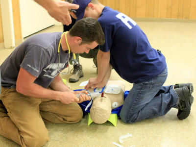 Two individuals practicing CPR on a training dummy.