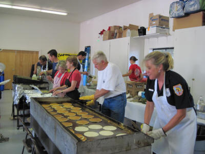 People cooking pancakes on a large griddle in a community or event setting.