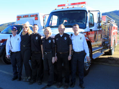 Group of firefighters posing in front of fire trucks.