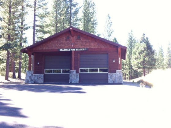 A red fire station with two garage doors surrounded by trees.