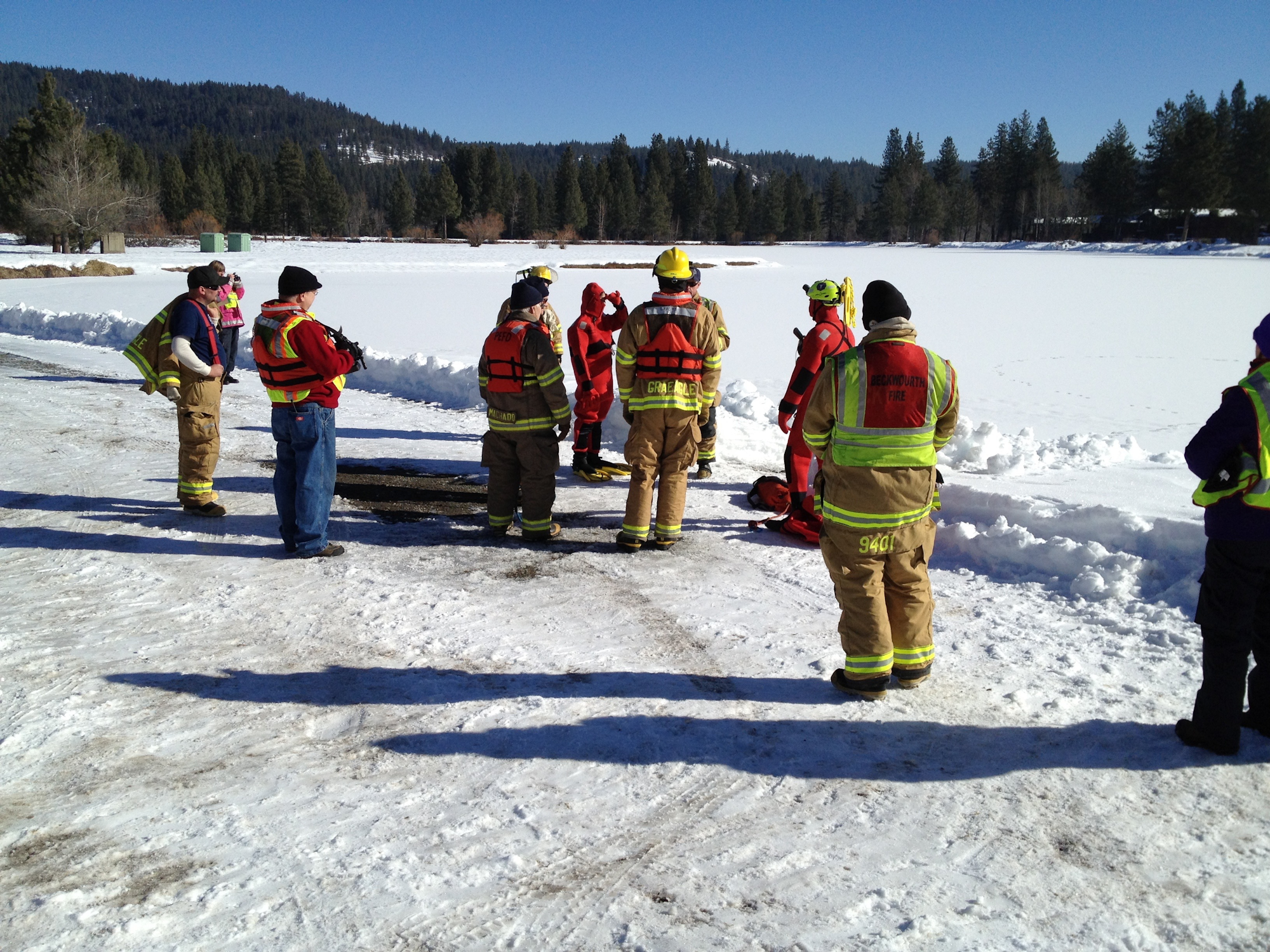 Firefighters training on a snowy field with trees in the background.