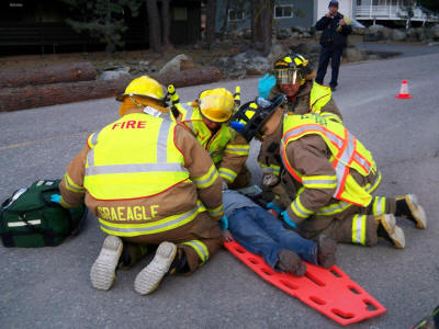 Firefighters attending to a person on a stretcher, emergency response in action, with medical equipment and a bystander observing.