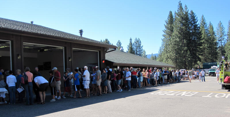 A long line of people waiting outside a building on a sunny day.