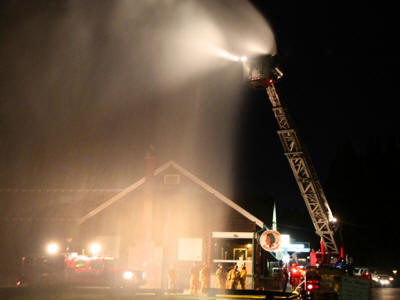 Firefighters using a ladder truck to douse a fire at night.