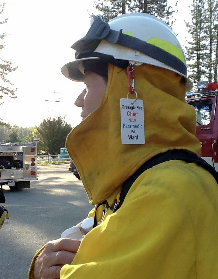 A firefighter in yellow turnout gear and helmet with a fire truck in the background.