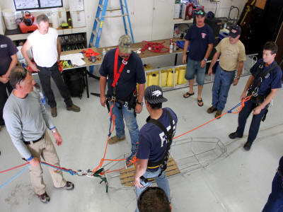 A group of people in a workshop, possibly a training session involving safety equipment and harnesses.