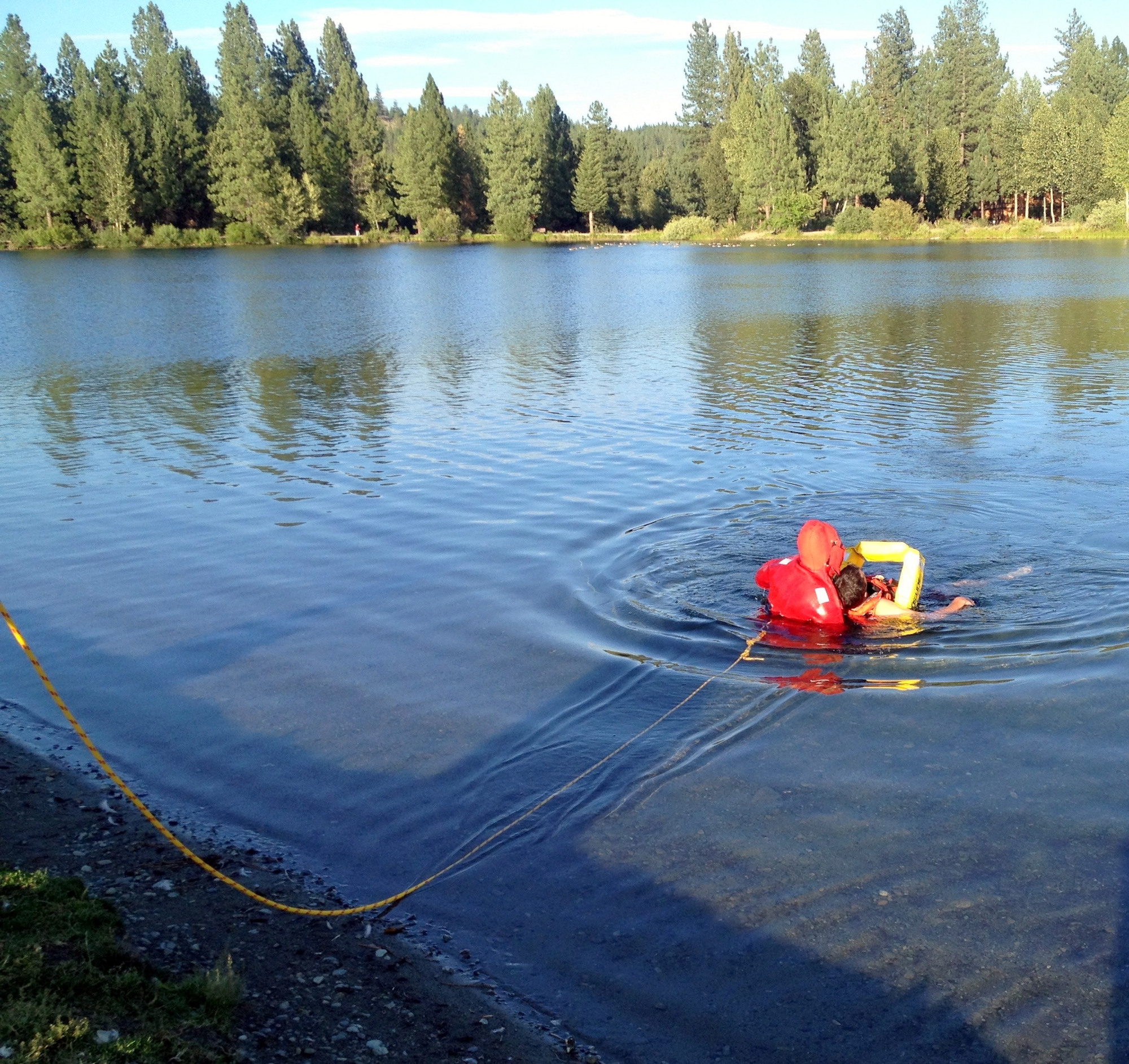 Person in red life jacket training with a rescue dummy in a lake, with trees in the background.