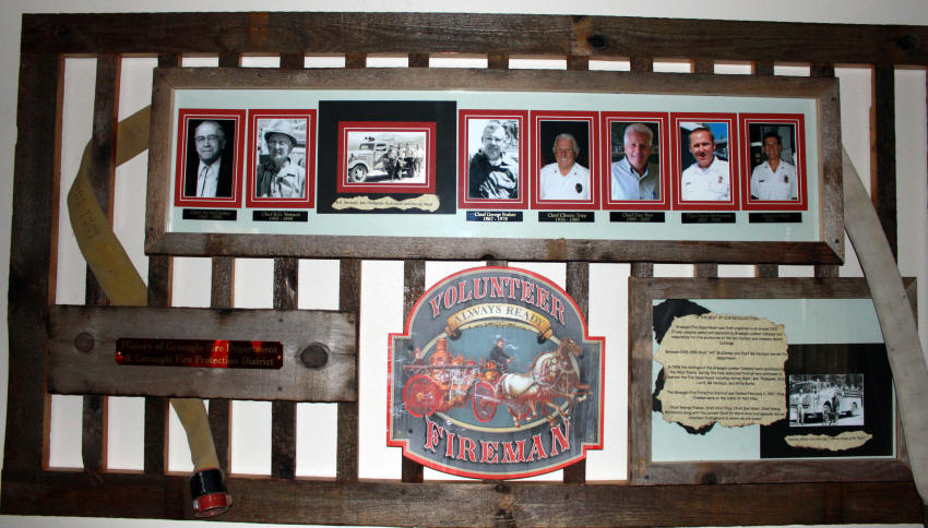 A display with photos, a "Volunteer Fireman" sign, an old fire nozzle, and a framed worn document, likely honoring firefighters.