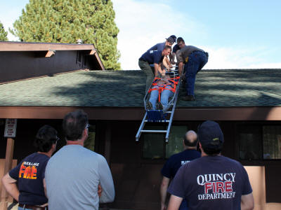 Firefighters and onlookers by a ladder and a rooftop.