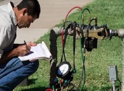 A person is taking notes beside some industrial gauges and pipes outdoors.