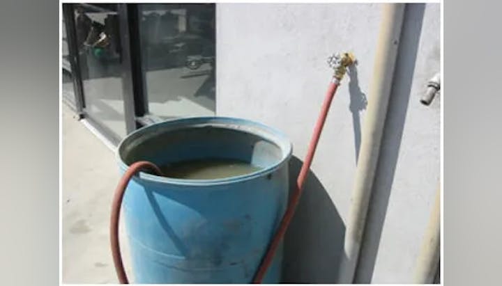 A blue bucket with water connected to a hose, against a wall.