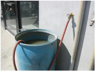 A blue bucket with water connected to a hose, against a wall.