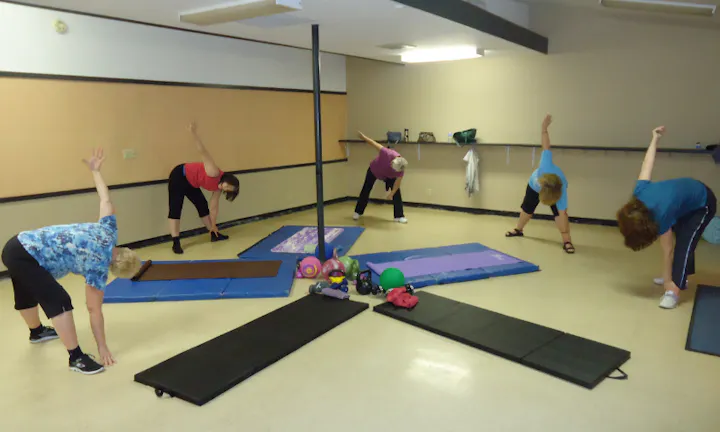 A group of people are stretching and exercising in a fitness studio with mats and weights.