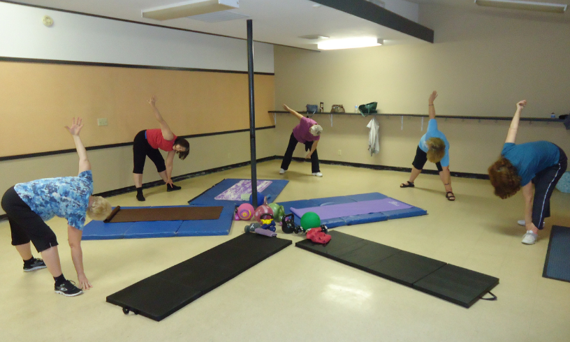 A group of people are stretching and exercising in a fitness studio with mats and weights.