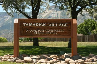 Sign for Tamarisk Village, a covenant-controlled neighborhood, surrounded by trees and mountains in the background.