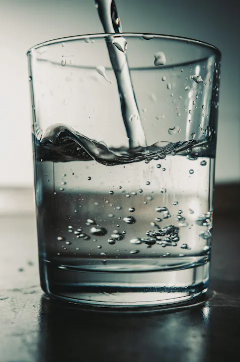 A glass filled with water is being poured, creating bubbles and ripples on the surface.