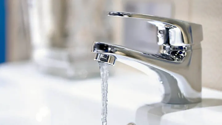 A chrome faucet with running water, likely in a bathroom.