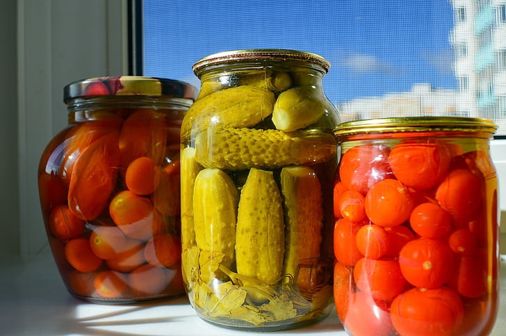 Three jars filled with pickled vegetables: cucumbers and tomatoes on a sunny windowsill.