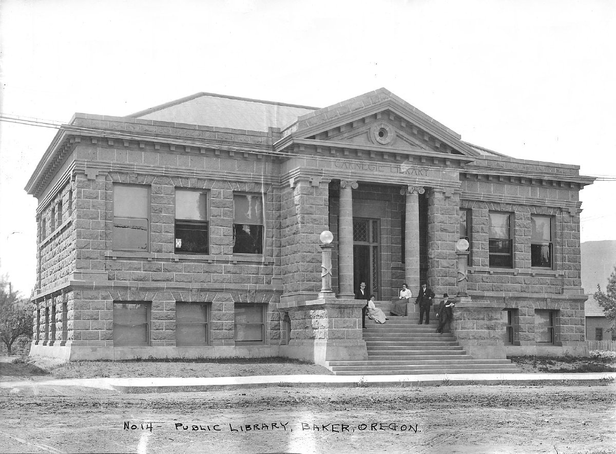 A historic photo of the Carnegie Public Library in Baker, Oregon, featuring people seated on the steps outside.