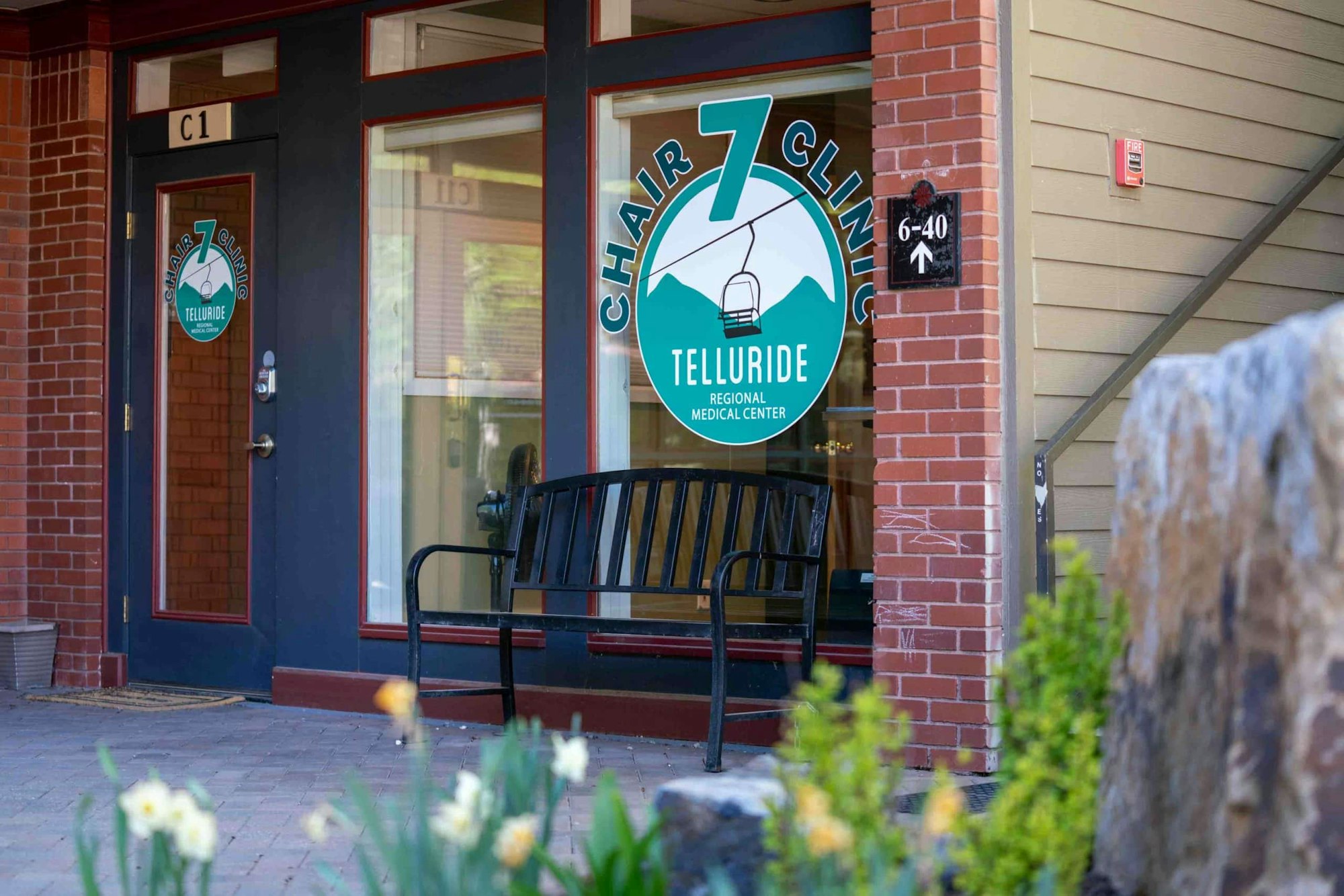 Entrance to Chair 7 Clinic, Telluride Regional Medical Center with a black bench and flowers in the foreground.