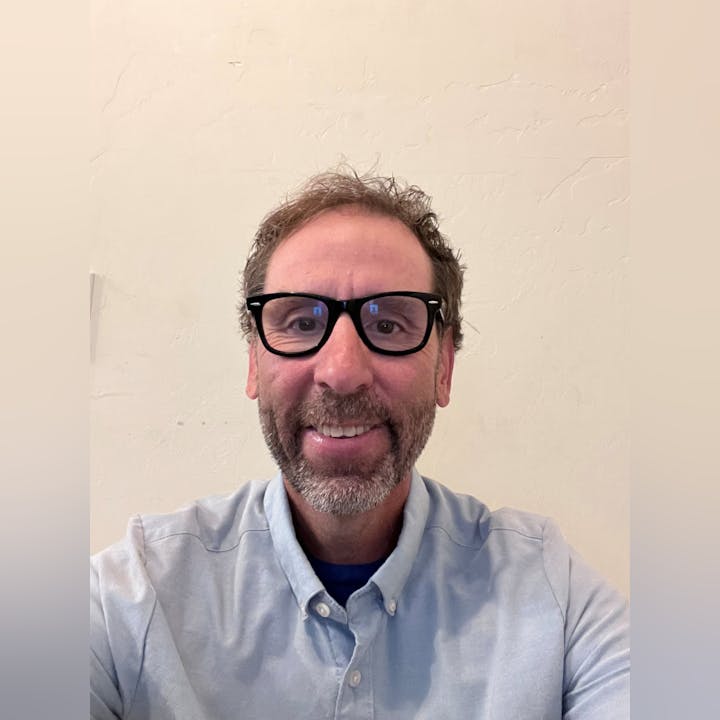 A person wearing glasses and a button-up shirt, smiling at the camera.
