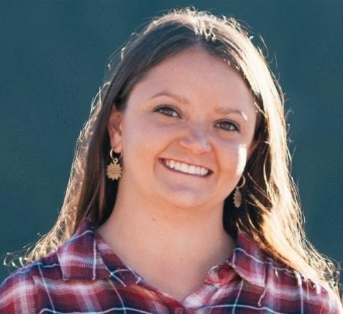 A person smiling, wearing a red plaid shirt and earrings, with long hair.