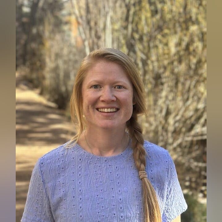 Person smiling outdoors, wearing a blue top with braided hair.