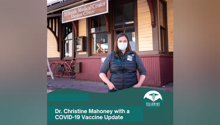 A masked woman stands in front of Telluride Medical Center Depot Clinic with a COVID-19 vaccine update message.