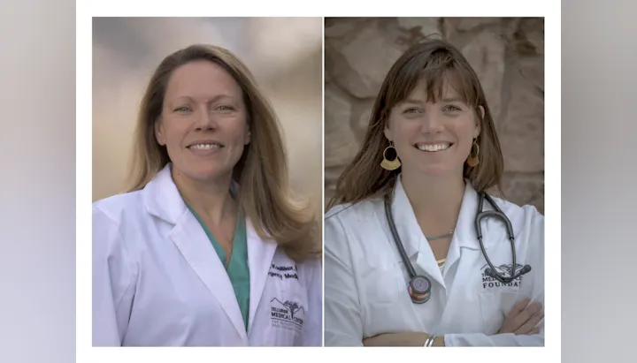Two women in white medical coats standing side by side, smiling.