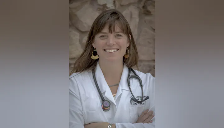 A person wearing a white coat with a stethoscope around their neck, smiling.