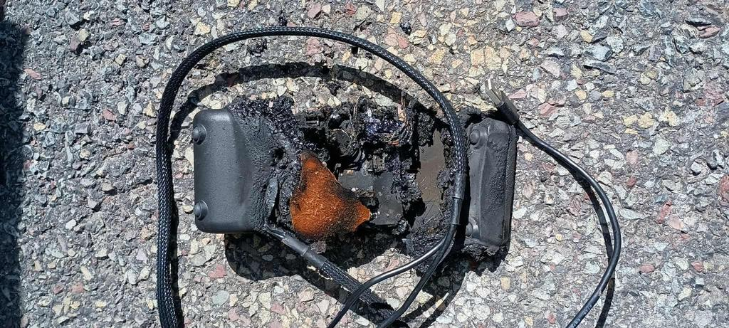 A melted and burnt electronic device on a rough asphalt surface.