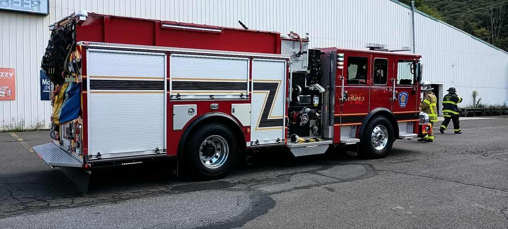 A red fire truck parked with firefighters nearby, in front of a large building.