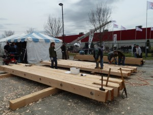People working on large wooden beams near a tent at an outdoor site.