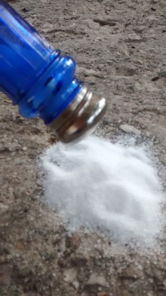 A blue salt shaker spilling salt onto a stone surface.