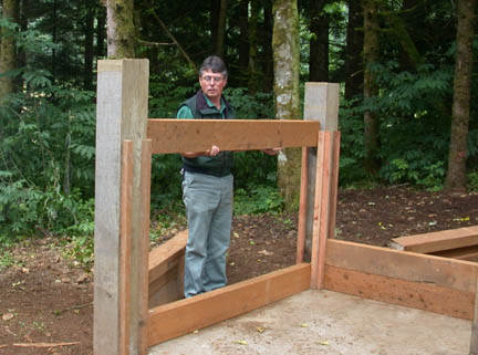 A person assembling a wooden structure in a forest setting.