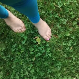 Bare feet with painted toenails stand on grass, next to blue leggings.