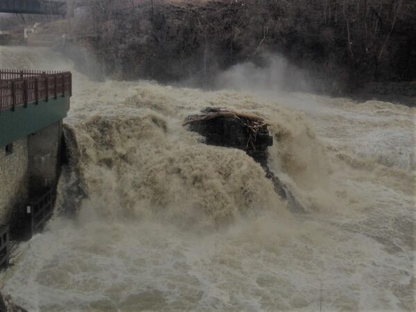 A powerful waterfall with turbulent water crashing over rocks, surrounded by mist.
