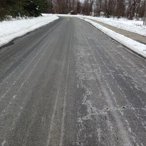 Icy road with snow-covered sides and a tree-lined background.