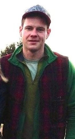 A person wearing a cap and layered clothing, standing outdoors.