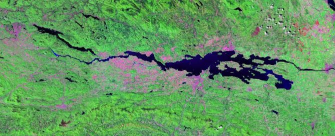Satellite image showing a green landscape with water bodies, likely lakes or rivers, and some areas highlighted in pink and purple.