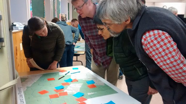 A group of people examines a map on a table, with colorful sticky notes placed on it.