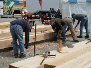 People working with large wooden beams outdoors, using tools.
