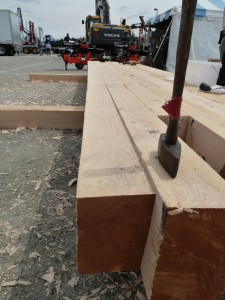 Large wooden beams, chisels, and machinery outdoors at a construction site or event.