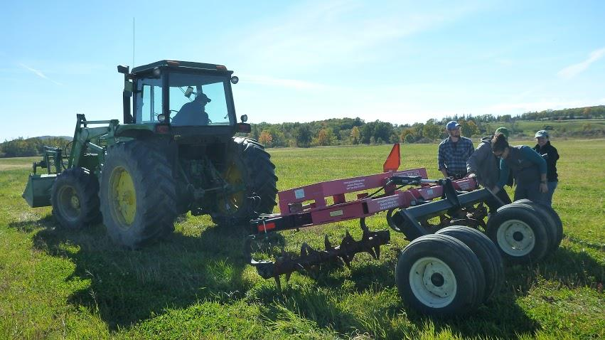 A tractor and people standing next to farming equipment in a field.