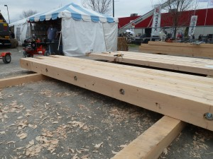 Large wooden beams laid on the ground near a tent, with wood shavings scattered around.