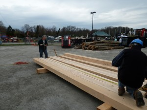Two people measuring and working with large wooden beams outdoors.