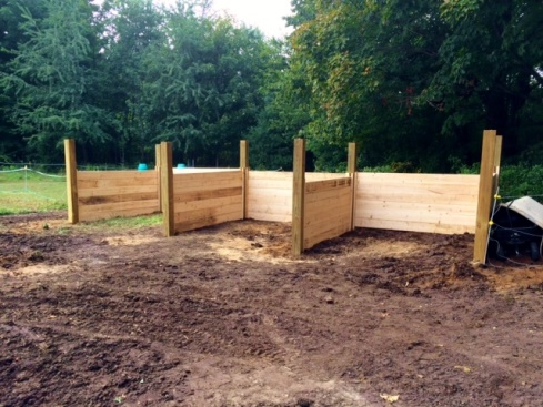 Wooden compost bins under construction in a garden area with trees in the background.