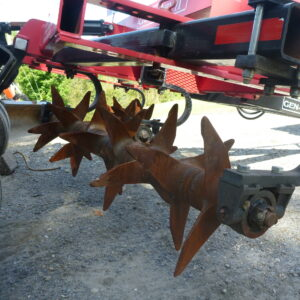 Close-up of a red agricultural machine with rotating metal blades for soil cultivation.