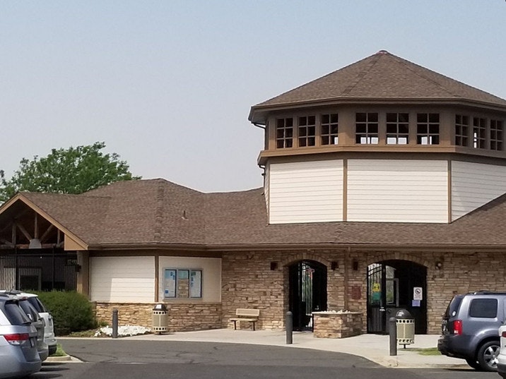 Building with a circular tower, stone and wood exterior, cars in the parking lot, trees in the background.
