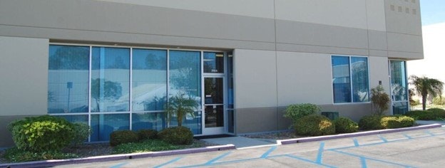 Office building entrance with reflective windows and landscaped bushes.